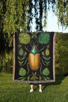 a woman standing in the grass holding up a blanket with a beetle on it