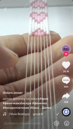 a person holding a string with beads on it's fingers and the strings are white, pink, and blue