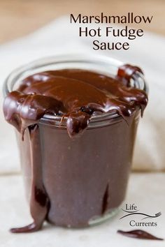 a glass jar filled with chocolate sauce on top of a white tablecloth and text overlay reads marshmallow hot fudge sauce