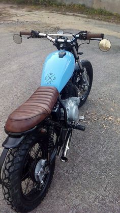 a blue motorcycle parked on top of a parking lot next to a building with a brown leather seat