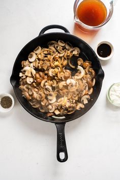 a skillet filled with cooked mushrooms and seasoning next to other ingredients on a white surface