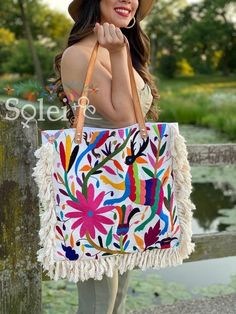 a woman wearing a hat and carrying a colorful bag with fringes on the handles