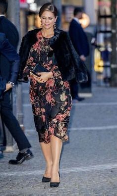 a woman walking down the street in a floral dress and fur stoler, with her hand on her hip