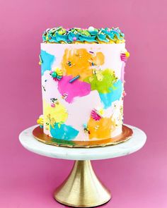 a multicolored cake with sprinkles on top sits on a gold pedestal