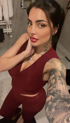 a woman in a red dress posing for the camera with tattoos on her arms and shoulder