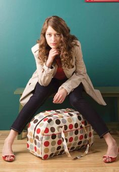 a woman sitting on top of a polka dot duffel bag with her hand under her chin