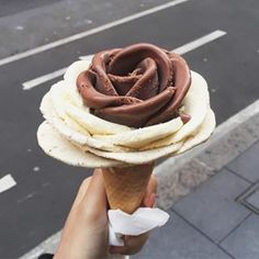 a person holding an ice cream cone with chocolate frosting on it's top