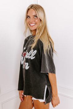 - Sparkle on the sidelines with this adorable 'FOOTBALL MOM' top! Perfect for showing your team spirit, this piece is comfy-casual style with a touch of glam. Its eye-catching design makes it a must-have for every proud football mom. - Unlined sweatshirt material with a vintage wash - A white and red hued 'FOOTBALL MOM' graphic design with rhinestone accents - Unfinished seam accents - A crew cut neckline - Short, loose sleeves - An ultra-relaxed silhouette that ends in a high-low hemline with s Black Embroidered Graphic Tops For College, Black Embroidered Tops For College, Black Tops With Embroidered Graphics For Fall, Black Embroidered Tops For Fall, Black Tops For Game Day With School Spirit, Black Varsity Top For Game Day, Sporty Black Tops With Embroidered Graphics, Black Collegiate Tops For Fall, Trendy Black Tops For Game Day