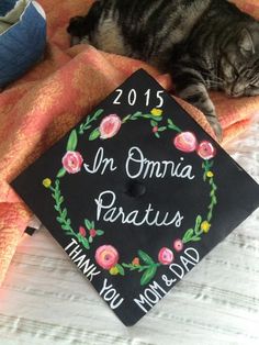 a cat laying on top of a graduation cap that says in omma paratus thank you mom and dad