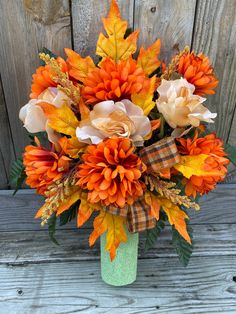 a vase filled with orange and yellow flowers on top of a wooden table next to a fence