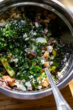 a bowl filled with vegetables and feta cheese on top of a wooden table next to a spoon