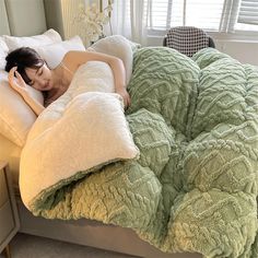 a woman laying in bed on top of a green comforter with pillows and headphones