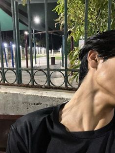 a woman sitting on a bench in front of a fence at night with her eyes closed