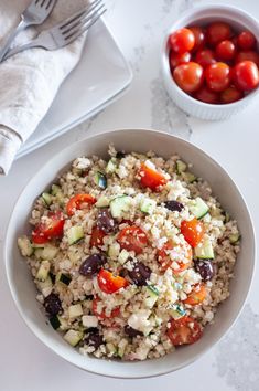 a white bowl filled with rice, tomatoes and cucumbers next to a fork