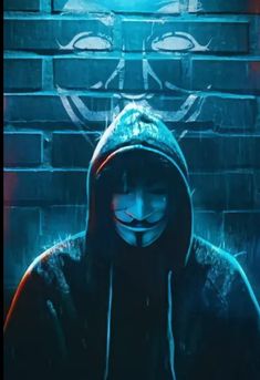 a person wearing a mask and hood in front of a brick wall with graffiti on it