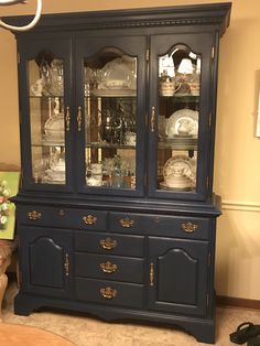 a blue china cabinet with glass doors and gold trimmings on the top shelf