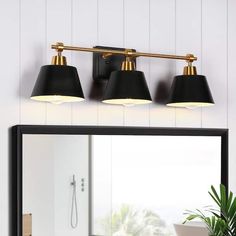 three light bathroom fixture with black shades and gold trim on the mirror in front of a white wall