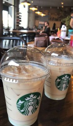 two starbucks drinks sitting on top of a wooden table next to each other in plastic cups