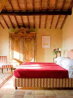 a bed sitting under a wooden ceiling next to a chair and table in a bedroom