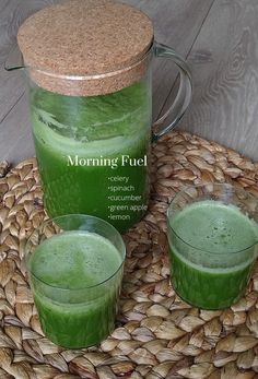 two glasses filled with green liquid sitting on top of a woven place mat next to a jug