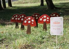 four red mushrooms with white polka dots are in the grass near a sign that says forest is for mushroom ring toss