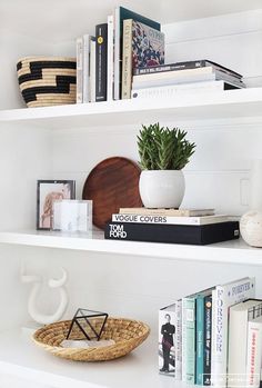 some books and plants are on the shelves in this white bookcase with wicker baskets