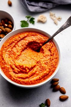 a bowl of red sauce with almonds and parsley on the side next to it