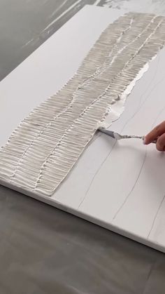 a person using a paintbrush to paint a piece of white paper with lines on it