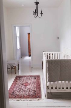 a baby crib in a white room with a chandelier hanging from the ceiling