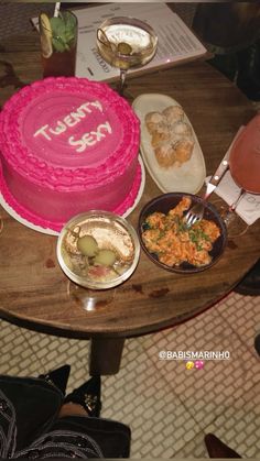 a pink cake sitting on top of a wooden table next to other plates and bowls