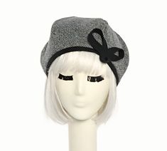 a white mannequin head wearing a gray hat with black ribbon and bow on it