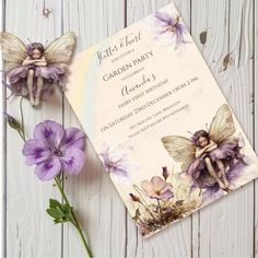 a purple flower next to a card with a fairy on it and two flowers in front of it