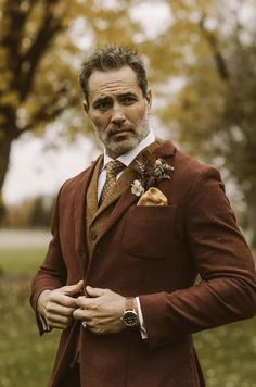 a man wearing a suit and tie standing in front of trees with leaves on it