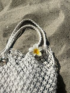 a white purse with a yellow flower on it sitting in the sand at the beach