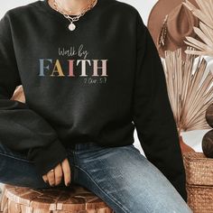 a woman sitting on a stool wearing a black sweatshirt with the words faith printed on it