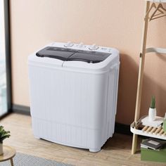 a white portable washing machine sitting on top of a wooden floor next to a window