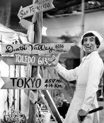 a woman standing next to a wooden sign with many signs on it's sides