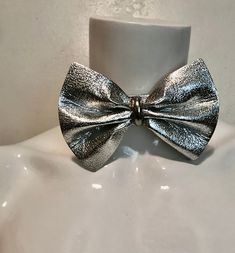 "1980's silver vinyl bow tie. Try it instead of a necklace...or all on its own Good size bow; 3 1/4\"h x 4 3/4\"w with metal center piece. Silver metal hook and chain at back allows for adjustments. No maker. Very good condition. total length 15\" strap 1\"w x 10 7/8\"l chain 3 1/2\"" Silver Bow Jewelry For Evening, Adjustable Bow Jewelry For Evening, Adjustable Bow Tie Jewelry For Party, Formal Silver Jewelry With Decorative Bow, Silver Satin Bow For Party, Elegant Silver Bow For Party, Silver Satin Party Bow, Adjustable Metallic Jewelry For Parties, Silver Bow Jewelry For Party