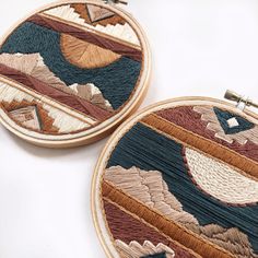 two hand embroidered hoops with mountains and clouds in them on a white table top