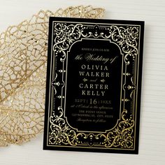 a black and gold wedding card with an ornate design on the front is next to a lace doily