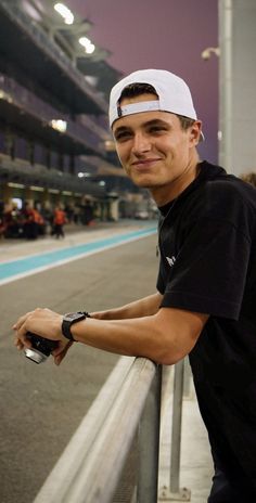 a man standing next to a metal rail near a race track at night with people in the background