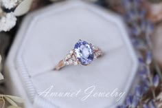 an oval shaped tan and white diamond ring sits on a box surrounded by lavender flowers