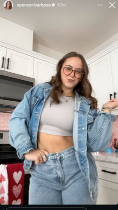 a woman wearing glasses and denim jacket standing in front of a kitchen counter with her hands on her hips