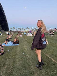 a woman walking across a grass covered field next to a large crowd at a music festival