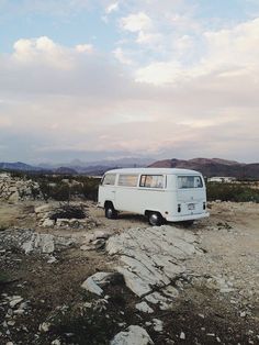 a white van parked on top of a dirt field next to rocks and grass with mountains in the background