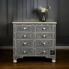 a white and black chest of drawers with flowers in vase next to it on wooden floor