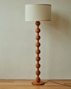 a wooden floor lamp with a white shade on the base and a light bulb attached to it