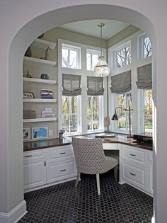 an arched doorway leads to a home office with built - in shelving and cabinets