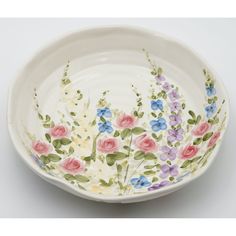 a white bowl with flowers painted on the side and green, pink, blue and purple flowers