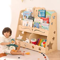 a little boy sitting on the floor holding a stuffed animal in front of a bookshelf